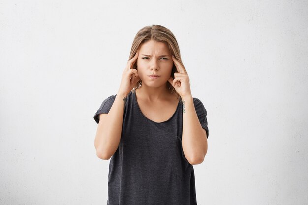 Isolated portrait of frustrated stressed out young mixed race female dressed in dark casual t-shirt holding fingers on her temples as if trying to remember something very important.