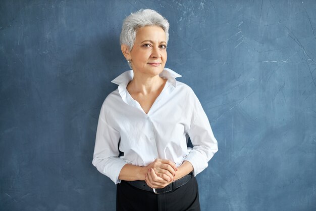 Isolated portrait of stylish experienced middle aged female executive with short gray hair standing in confident posture