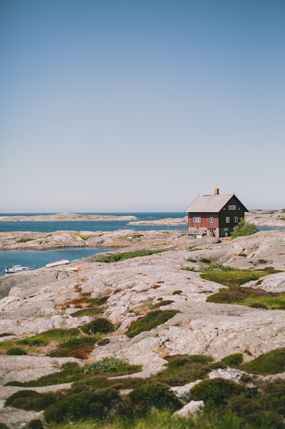 Free photo isolated red wooden house on the shore near the ocean under the blue sky on a sunny day