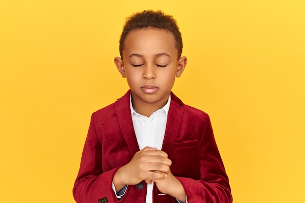 Isolated shot of African American little boy covering eyes and squeezing fist, trying to breathe deeply to calm down, loosing temper, being angry and furious.