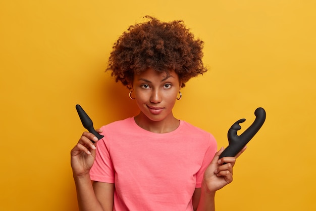 Isolated shot of african american woman poses with sex toys, uses butt plug for anal sex and rabbit vibrator to release sexual tension and boost your mood, increases sexual function gets self pleasure