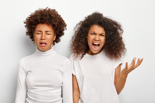 Isolated shot of angry displeased two ethnic sisters have failure, scream angrily