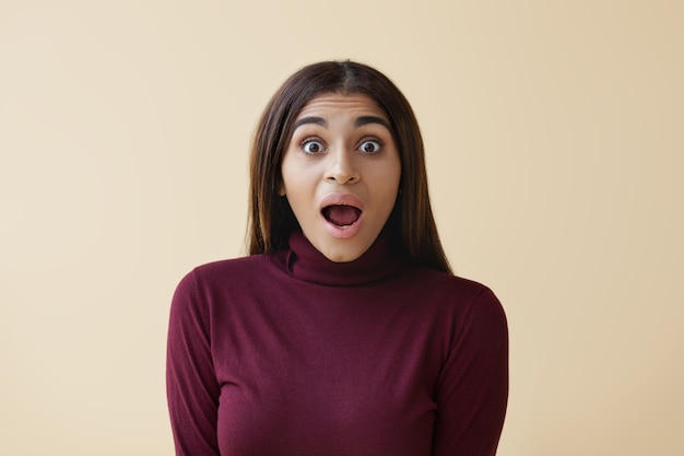 Isolated shot of beautiful Afro American woman with loose straight hair opening mouth widely, being lost for words, having surprised look, shocked with big sale prices or astonishing information