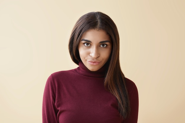 Free photo isolated shot of beautiful glamorous young woman in maroon turtle neck pouting lips while posing