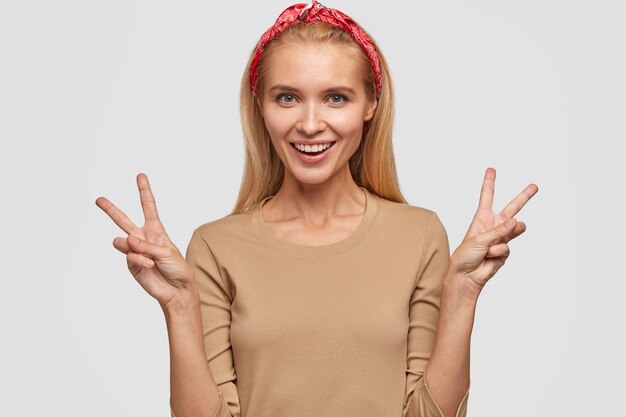 Isolated shot of cheerful blonde young woman posing against the white wall