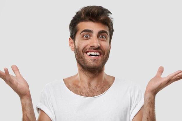 Isolated shot of cheerful gorgeous Caucasian man holds hands spread, rejoices good positive news or noticing someone