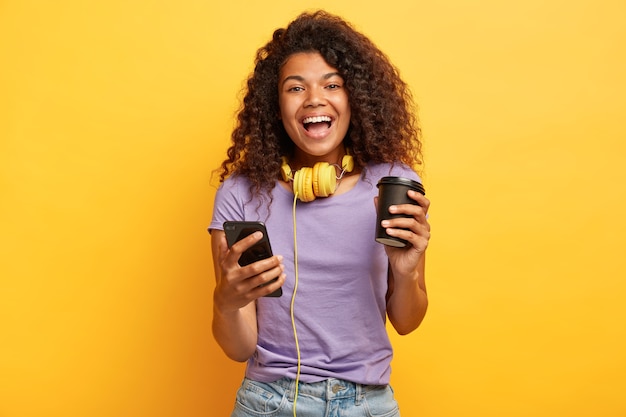 Isolated shot of delighted young female with afro hairstyle posing against the yellow wall