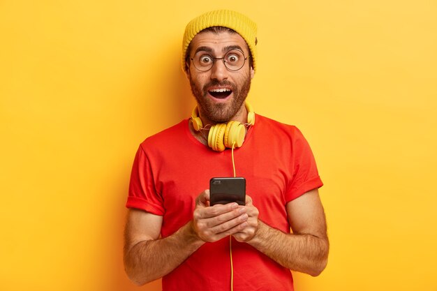 Isolated shot of excited surprised male shocked to get awesome video from friend, surfes web page on smart phone