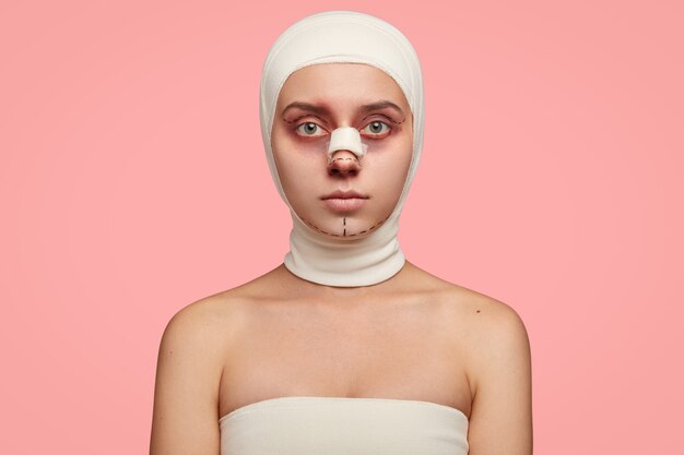 Isolated shot of girl has naked shoulders, face marked in lines, wrapped with bandage, prepared for facial treatment