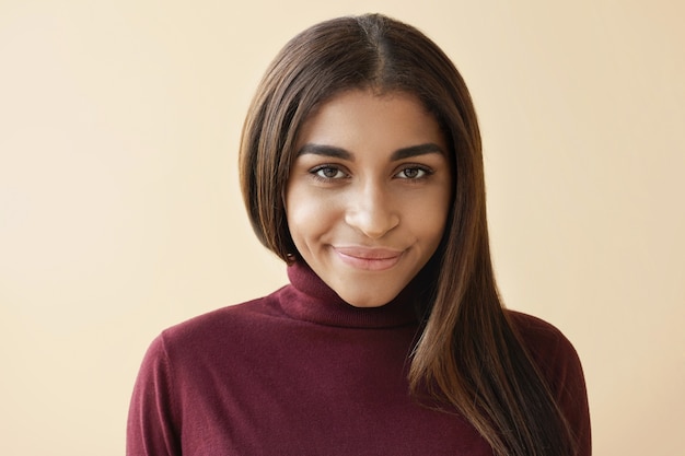 Isolated shot of gorgeous young African American female with healthy long hair and natural make up posing, looking with cute charming smile, rejoicing at some good positive news