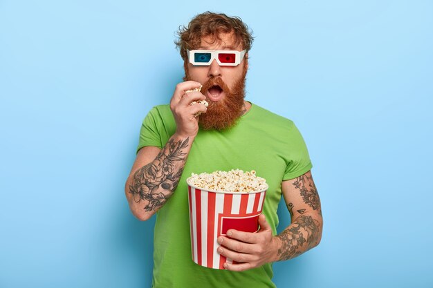 Isolated shot of handsome man has tattoo, ginger hair, watches movie, involved with story