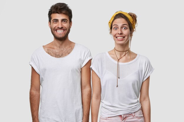 Изолированный снимок позитивных коллег со смешными счастливыми выражениями лиц, демонстрирующих белые зубы, широко улыбающихся, одетых в повседневную одежду, позирующих над стеной, выражающих счастье