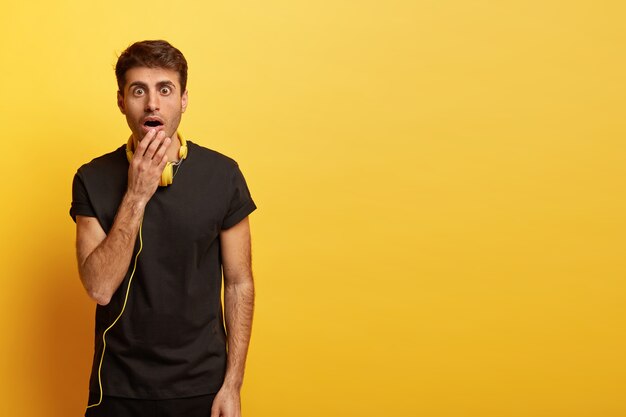 Isolated shot of scared Caucasian man keeps mouth widely opened, dressed in black t shirt