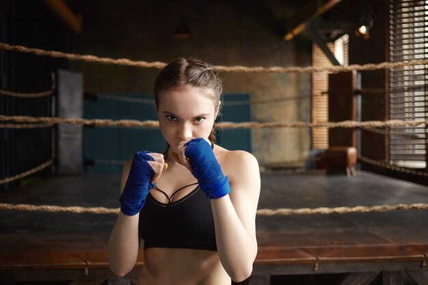 Isolated shot of self determined confident teenage girl training in gym, holding clenched fists in front of her