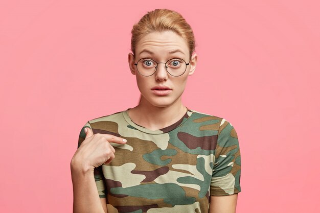 기절 한 매력적인 여성의 고립 된 총은 쇼핑몰에서 옷에 높은 가격에 놀란 새로운 티셔츠를 나타내며 핑크 스튜디오에 대해 포즈를 취합니다.