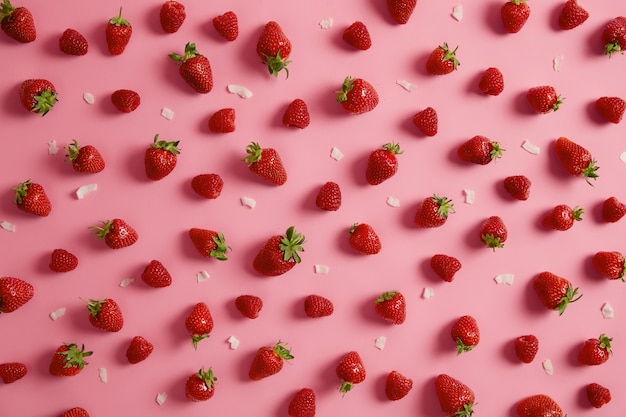 Isolated shot of tasty red strawberry with green stem isolated on pink background, coconut flakes around. Summer juicy fruit can be used in a variety of jams, jellies, and desserts, addition to diet