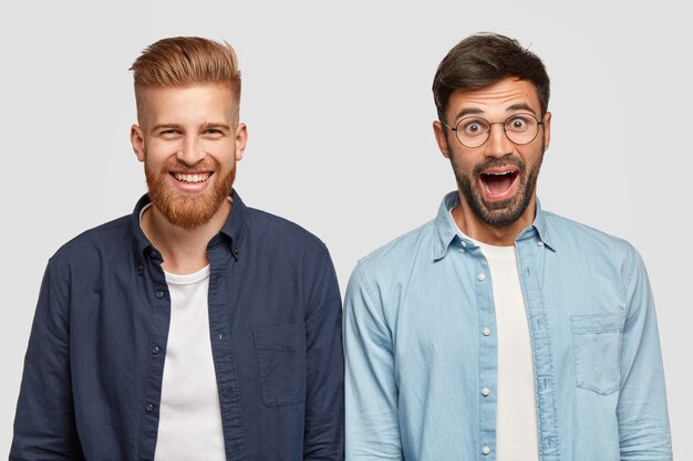 Isolated shot of two joyful surprised bearded guys express positive emotions