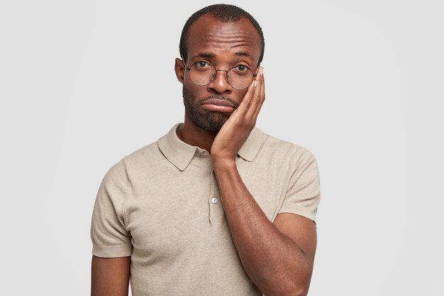 Isolated shot of unhappy African American male purses lips and looks desperately at camera