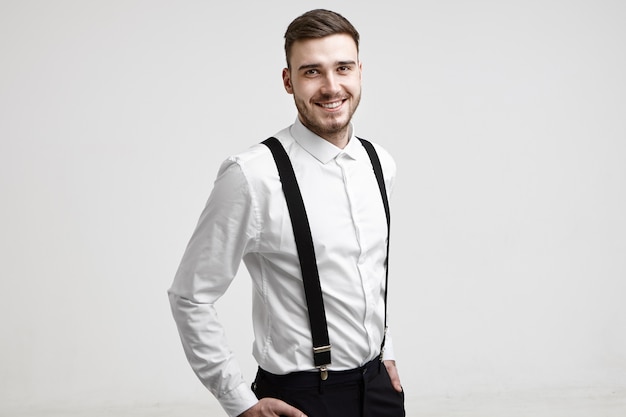 Isolated studio portrait of successful handsome young Caucasian businessman with trimmed beard smiling happily at camera after he signed good contract. Business, success, style and fashion concept