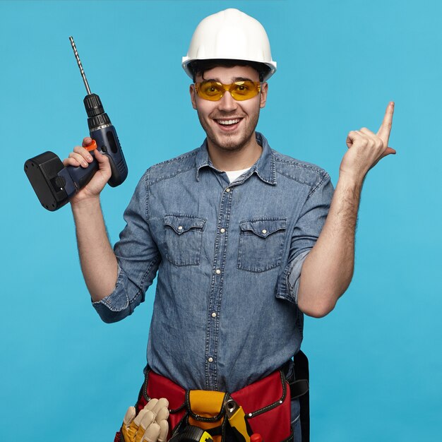 Isolated studio shot of cheerful emotional young repairman wearing protective goggles