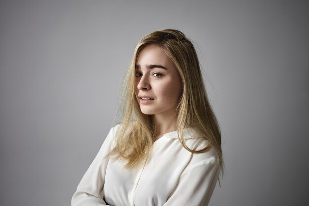 Isolated view of gorgeous beautiful young female office worker with loose hair having break during work day, posing against blank studio wall background with copy space for your information