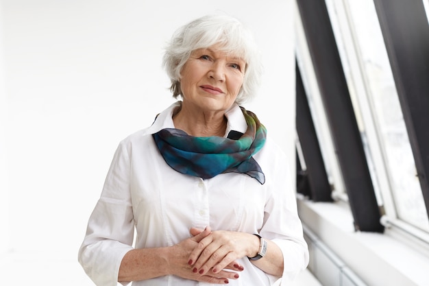 Isolated view of successful positive beautiful businesswoman with gray hair standing in confident posture
