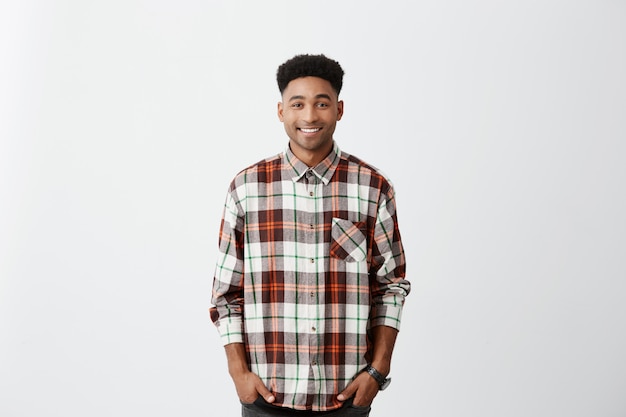 Free photo isolated on white wall. people and emotions. young good-looking dark-skinned man smiling, wearing checkered shirt with happy and relaxed face expression.