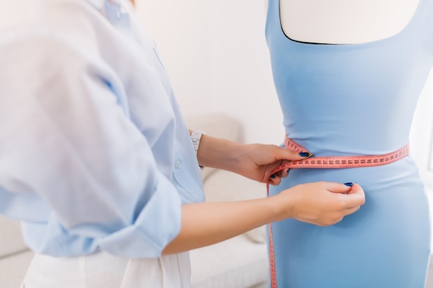 It is a picture where the main thing is concentrated on hands of a girl who makes fitting of dress on the mannequin. This picture is made in workshop studio.