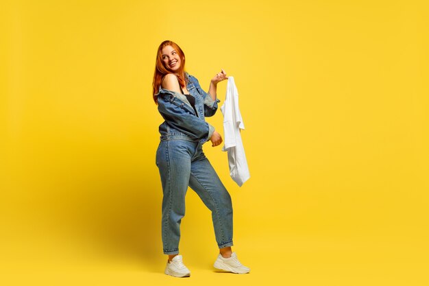 フォロワーになるのは簡単です。シャツが1枚だけの場合は、洗濯が速くなります。黄色の背景に白人女性の肖像画。美しい赤い髪のモデル。人間の感情、表情、販売、広告の概念。