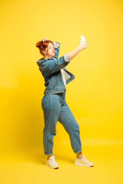 It's easier to be follower. Need minimum clothes for selfie. Caucasian woman's portrait on yellow background. Beautiful female red hair model. Concept of human emotions, facial expression, sales, ad.
