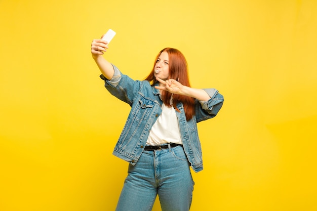 It's easier to be follower. Need minimum clothes for selfie. Caucasian woman's portrait on yellow background. Beautiful female red hair model. Concept of human emotions, facial expression, sales, ad.