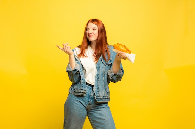 フォロワーになるのは簡単です。食べ物で写真を撮る必要はありません。白人女性は黄色の背景に。美しい女性の赤い髪のモデル。人間の感情、表情、販売、広告の概念。