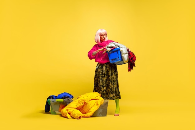 Free photo it's hard to be influencer. longer laundry with collection of clothes. caucasian woman's portrait on yellow background. beautiful blonde model. concept of human emotions, facial expression, sales, ad.