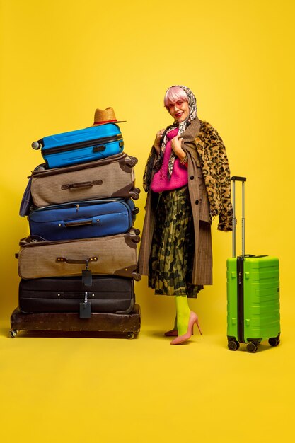 Трудно быть влиятельным лицом. Много одежды для путешествий. Портрет кавказской женщины на желтом фоне. Красивая блондинка модель. Концепция человеческих эмоций, выражения лица, продаж, рекламы.