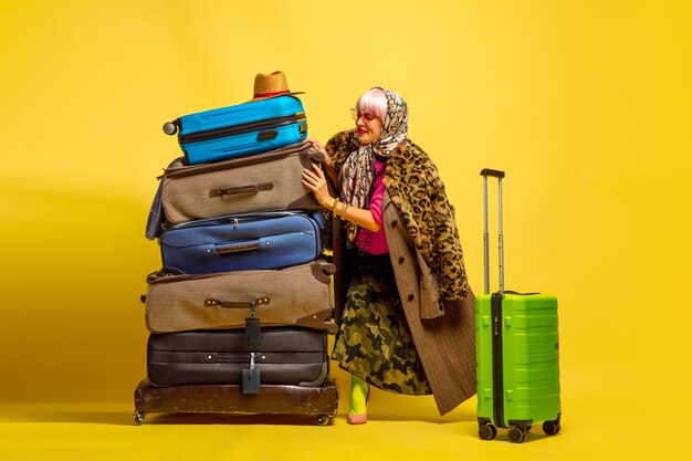 It's hard to be influencer. A lot of clothes for travel to go. Caucasian woman's portrait on yellow background. Beautiful blonde model. Concept of human emotions, facial expression, sales, ad.