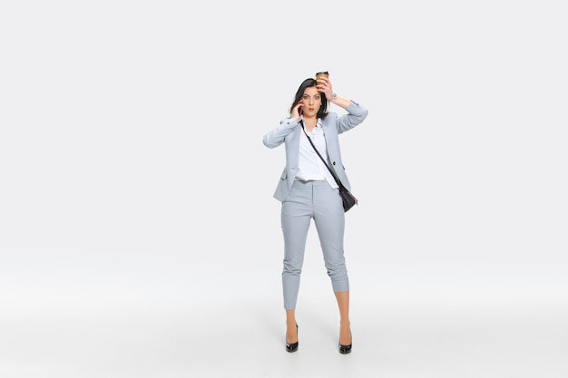 It's your headache now. Young woman in gray suit is getting shocking news from boss or colleagues. Looking numbed while dropping coffee. Concept of office worker's troubles, business, stress.
