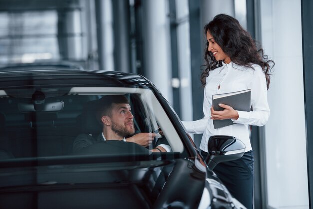 It's yours now. Male customer and modern businesswoman in the automobile saloon