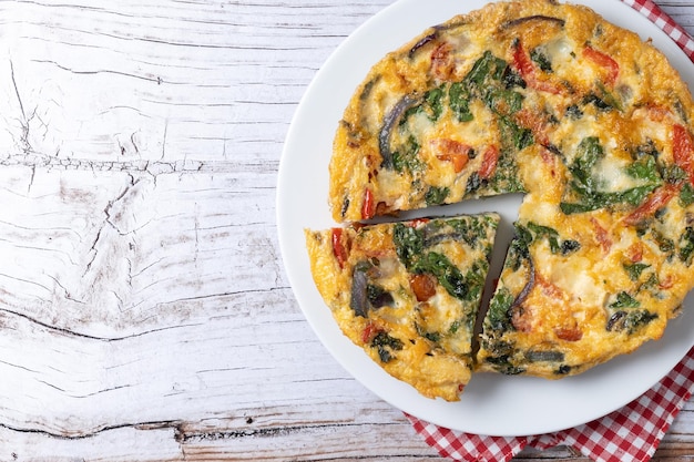 Italian Frittata made with spinach tomatoes onion and peppers on white wooden table