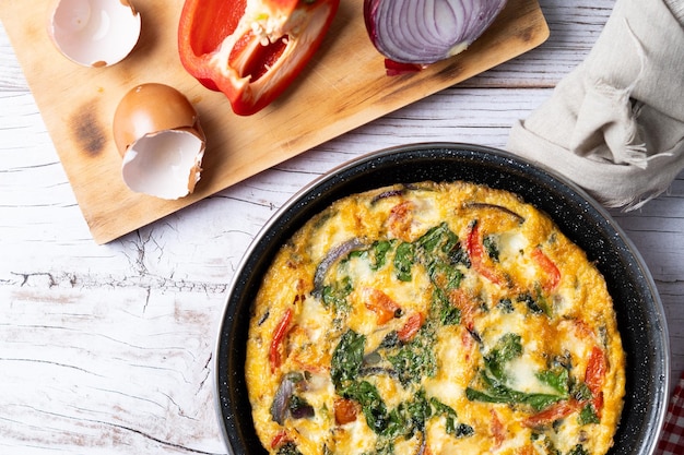 Foto gratuita frittata italiana fatta con spinaci, pomodori, cipolla e peperoni su un tavolo bianco di legno