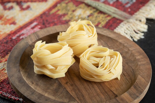 Italian rolled uncooked fettuccine pasta on wooden board with wheat