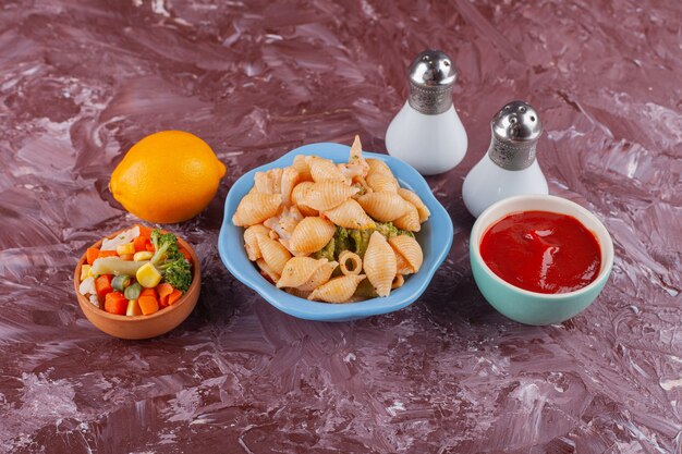 Pasta italiana delle coperture con salsa di pomodoro e insalata mista di verdure sul tavolo luminoso.