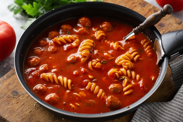 Итальянский томатный суп с макаронами из лапши и фрикадельками, приготовленными на сковороде. Крупным планом