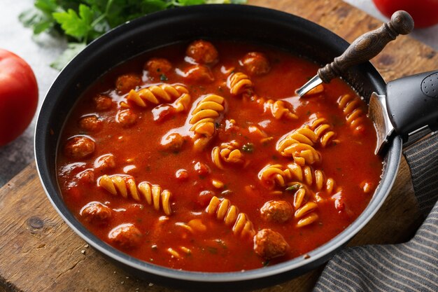 Italian tomato soup with noodles pasta and meatballs cooked in pan. Closeup