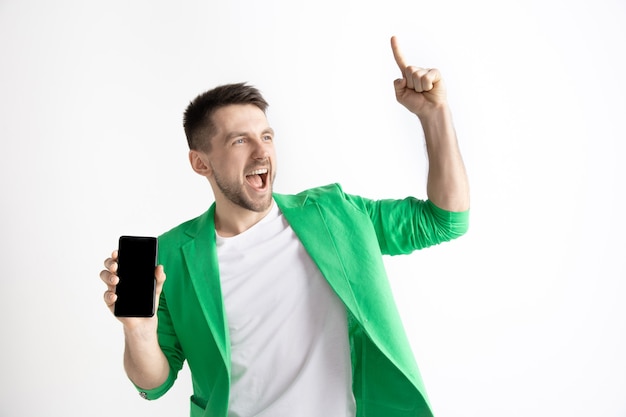 Its cool. Good news. Do that like me. Young handsome man showing smartphone screen and signing OK sign isolated on gray background. Human emotions, facial expression, advertising concept.