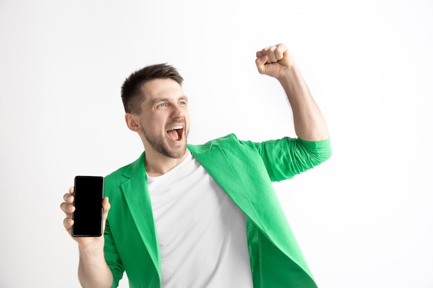 Free photo its cool. good news. do that like me. young handsome man showing smartphone screen and signing ok sign isolated on gray background. human emotions, facial expression, advertising concept.