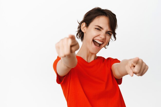 Its you congrats. Smiling cheerful girl pointing fingers, congratulating, inviting you to an event, standing in red t-shirt on white