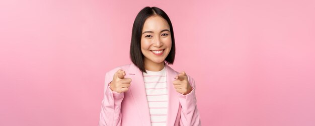 축하합니다 웃고 있는 열정적인 한국 기업 여성 사업가가 카메라를 가리키며 분홍색 배경 위에 서서 당신을 찬양하는 것을 축하합니다