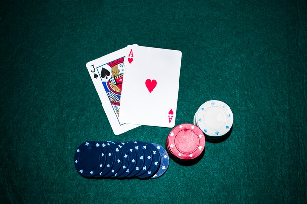 Jack of spade and heart ace card with casino chips stack on green poker table