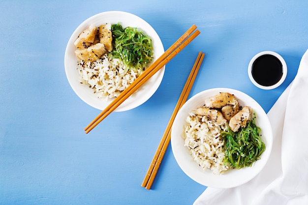 Японская еда. Чаша из риса, отварной белой рыбы и вакаме чука или салат из морских водорослей. Вид сверху. Плоская планировка