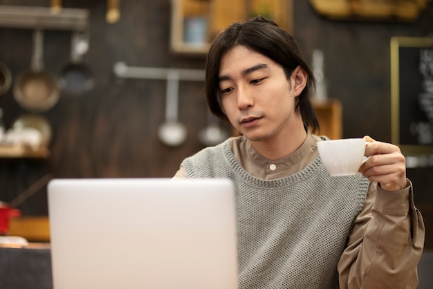 Uomo giapponese che beve caffè e lavora al suo computer portatile in un ristorante